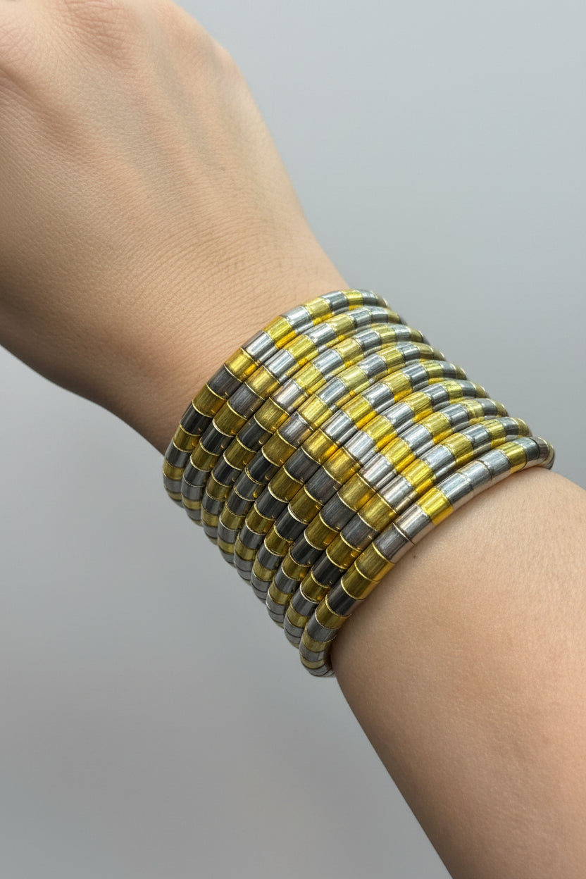 A close-up of a person's wrist wearing a wide cuff bracelet made of stacked translucent yellow, gold, and silver disc-like beads, with a second matching bracelet partially visible behind it.
