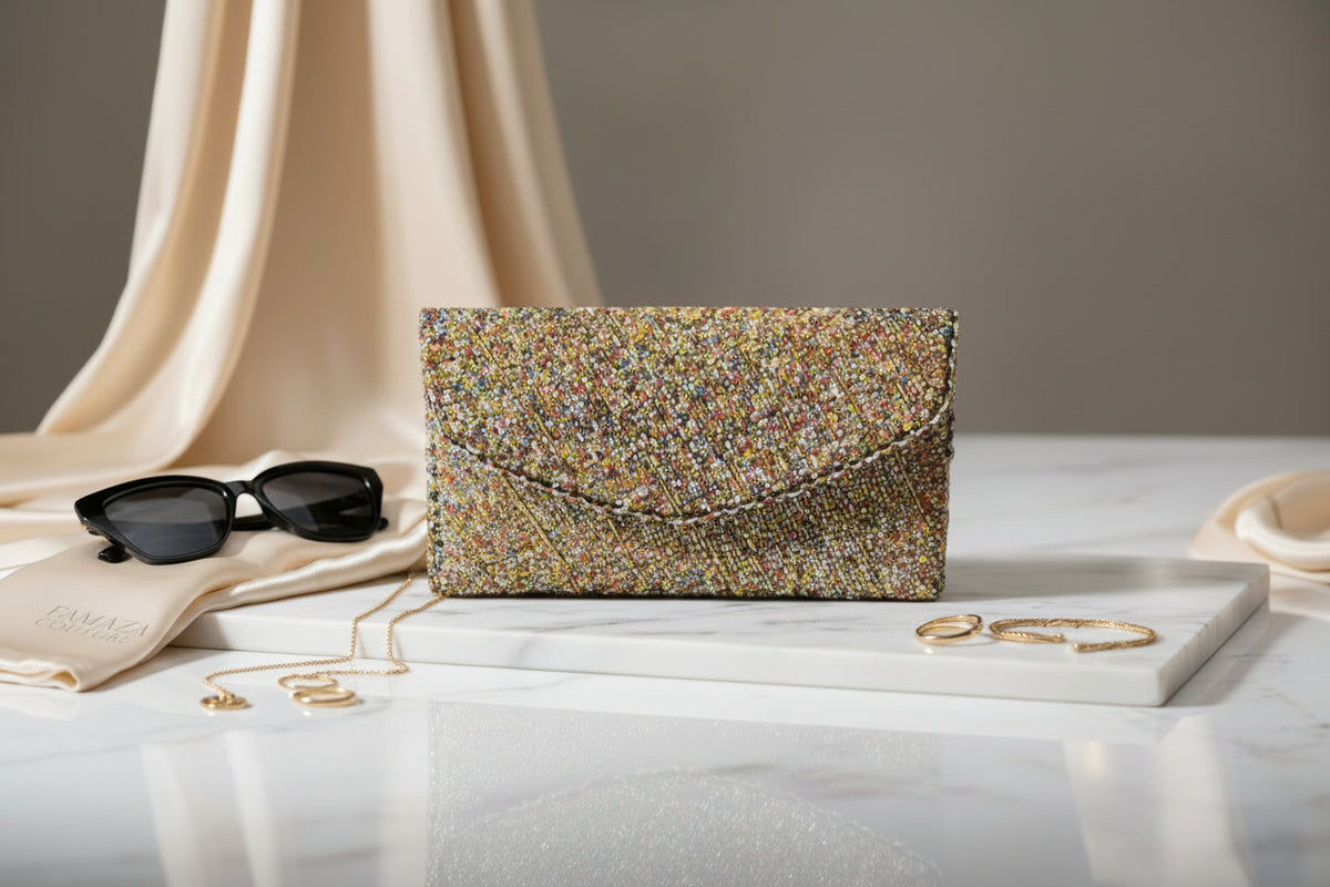 A clutch bag with a light base covered in multi-colored nano glass beads, displayed on a wooden surface surrounded by green leaves.