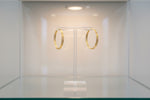 A crisp, professional studio photograph of the 10ct gold-plated baali earrings displayed on a luxury jewellery T-bar stand, showcasing the high-polish finish and the uniform curvature of the brass base.