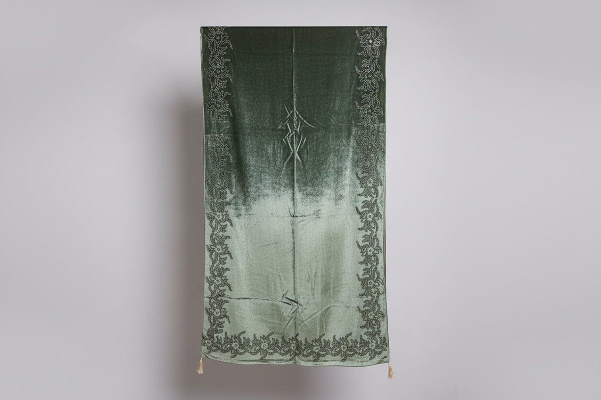 A draped apple green velvet stole in a dark colour, featuring intricate patterns and adorned with Swarovski work, displayed on a stand.