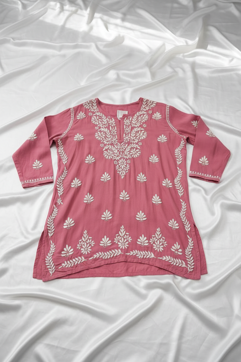A dusty rose pink long-sleeve tunic top with white floral block prints, hanging on a wooden hanger against a white marble background.