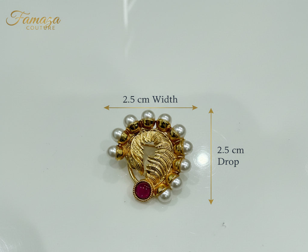 A gold-toned brooch featuring a stylized bird motif, surrounded by small white pearl-like beads and accented with a red oval stone, shown on a glossy light background.