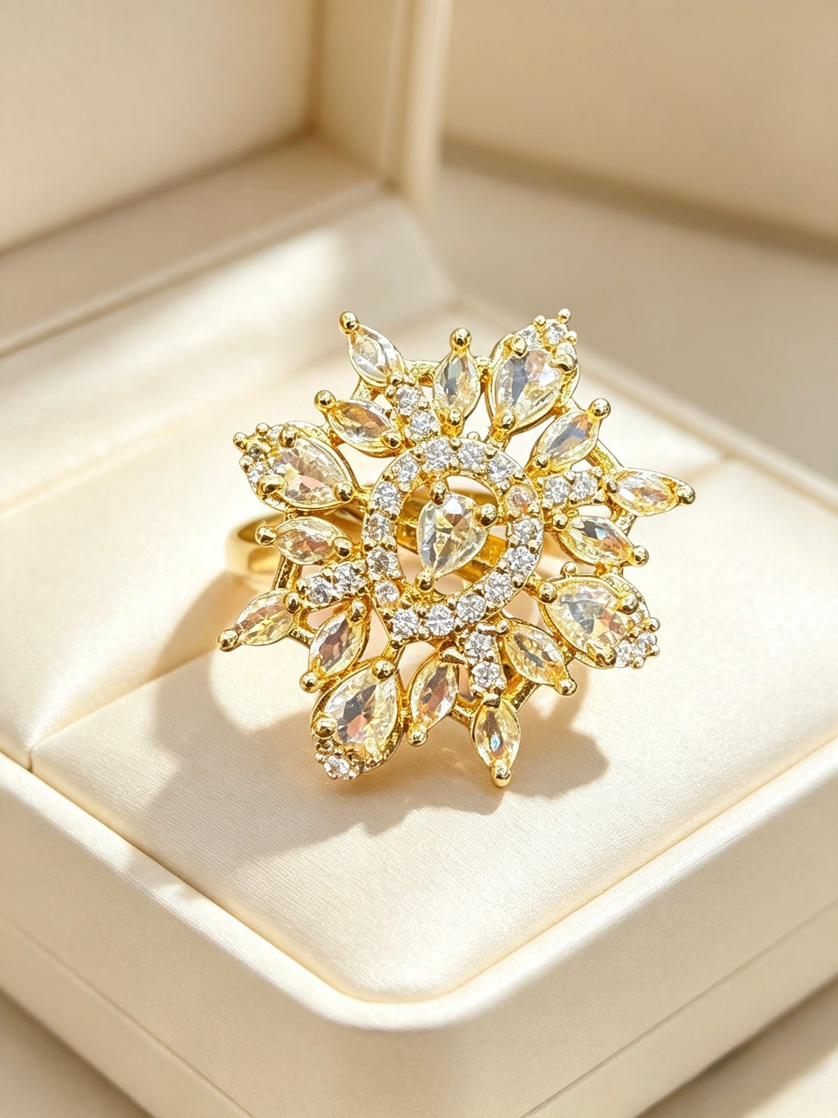 A gold snowflake-style ring with marquise and round clear crystals, displayed on a cream-colored jewelry box.