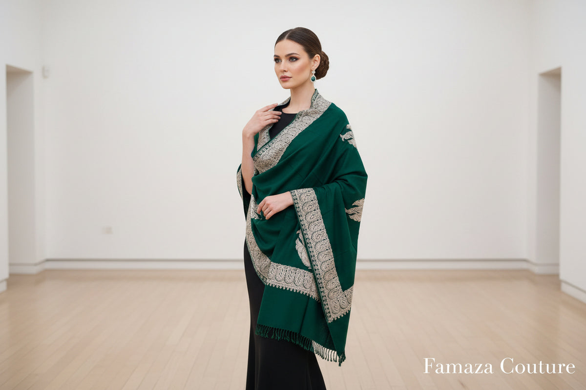 A green Kashmiri embroidered pashmina scarf with tassels on the ends, displayed on a wooden surface.