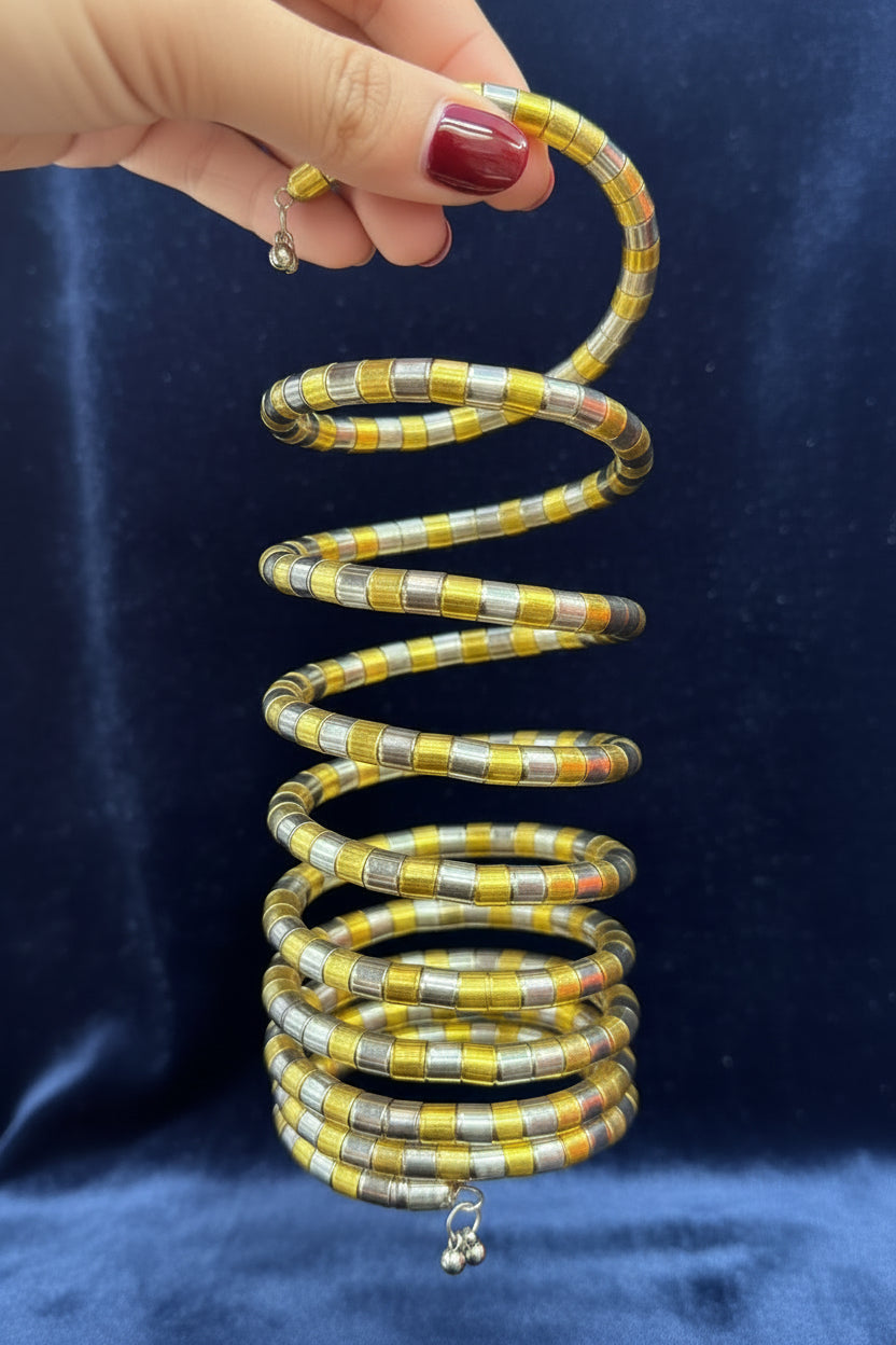 A handmade beaded coiled spring necklace with yellow, silver, and orange-red beads, held by a hand against a black fabric background.