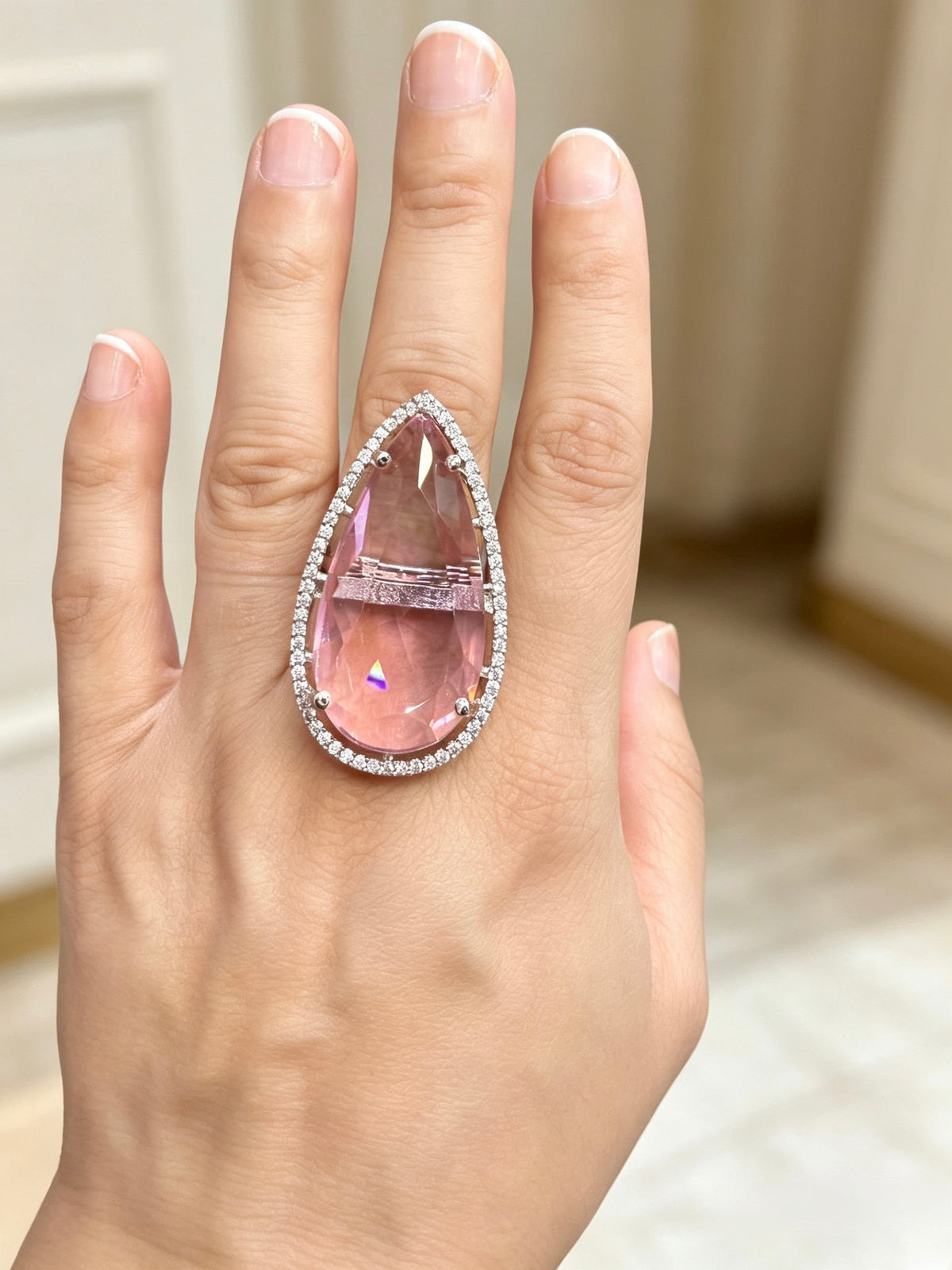A large teardrop-shaped pink gemstone ring with a diamond halo, worn on a person's hand.