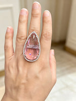 A large teardrop-shaped pink gemstone ring with a diamond halo, worn on a person's hand.