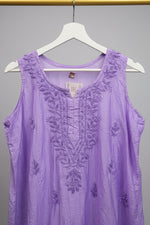 A lavender purple sleeveless tunic top with matching embroidered lace detailing on the neckline and scattered floral motifs, hanging on a white hanger in a retail setting.