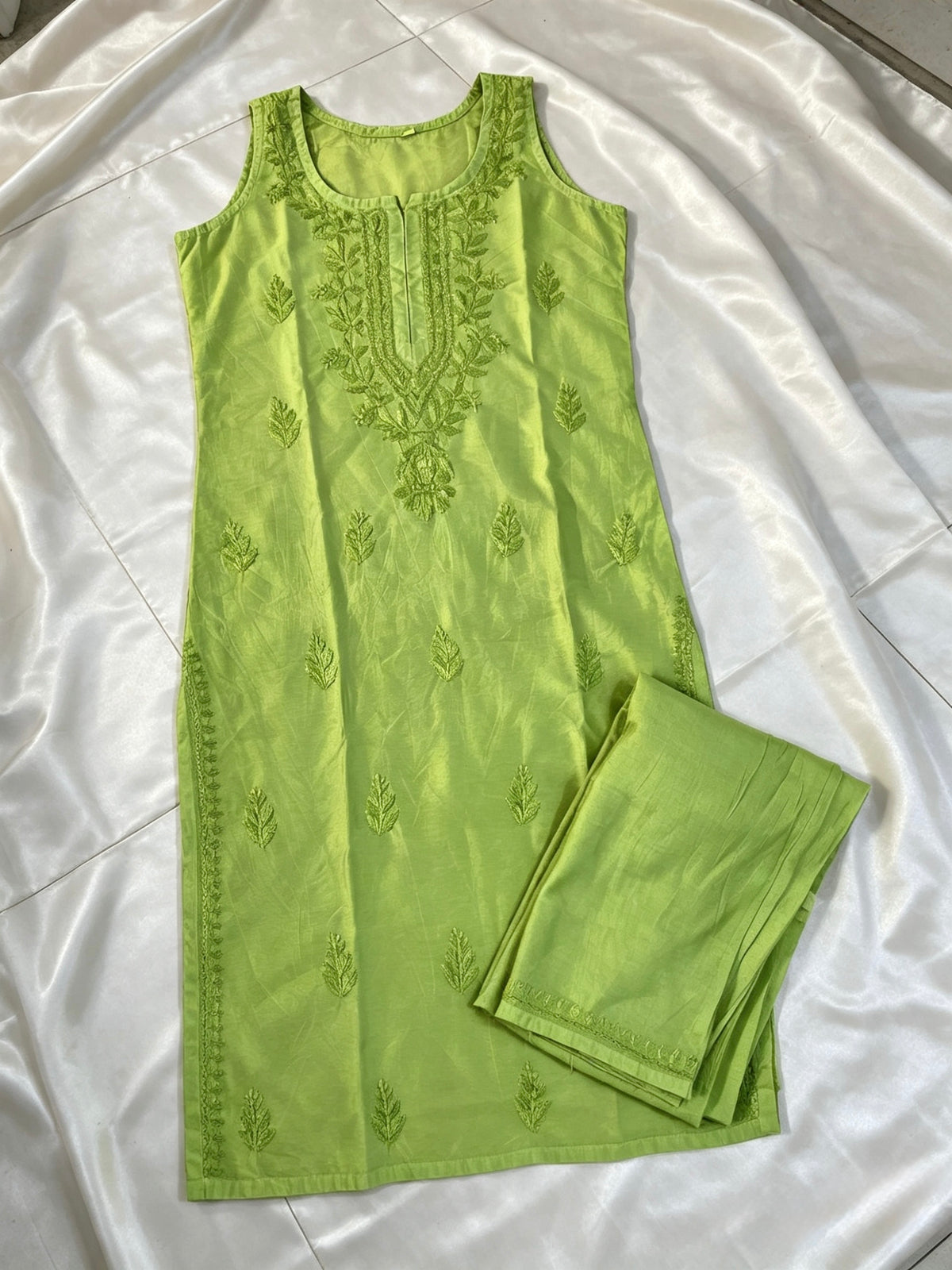 A light green sleeveless kurta with matching embroidered pants, laid flat on a white satin fabric background.