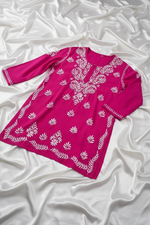 A magenta pink long-sleeve tunic top with white floral and leaf embroidery, hanging on a white hanger against a white background.