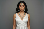 A mannequin showcasing a necklace set with bottle green and white stones, accompanied by earrings and a maang tikka. Party wear set. 