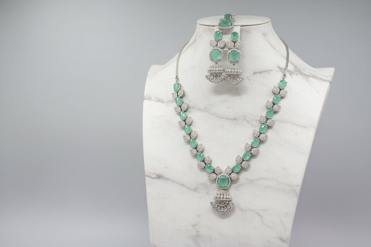 A mannequin showcasing a necklace set with green and white stones, accompanied by earrings and a maang tikka. Party wear AD set. 