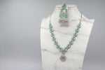 A mannequin showcasing a necklace set with green and white stones, accompanied by earrings and a maang tikka. Party wear AD set. 