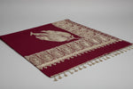 A maroon colour Kashmiri embroidered pashmina shawl with tassels on the ends, displayed on a wooden surface.