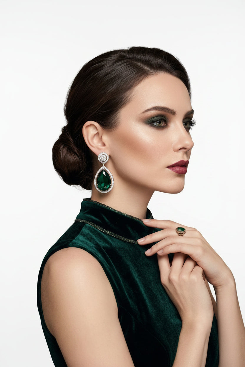 A model wearing elegant pear-cut emerald drop earrings with a diamond halo, styled with a matching green velvet dress.
