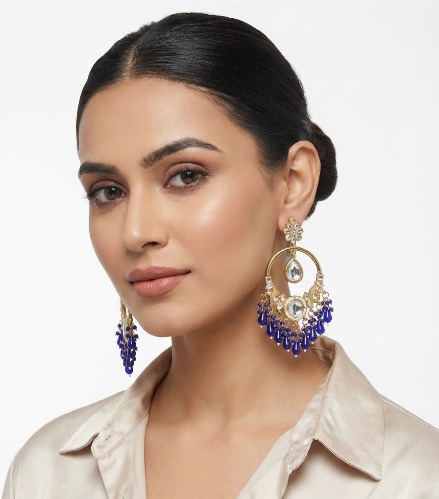 A model wearing large rose gold plated earrings featuring Kundan stonework and royal blue bead drops.