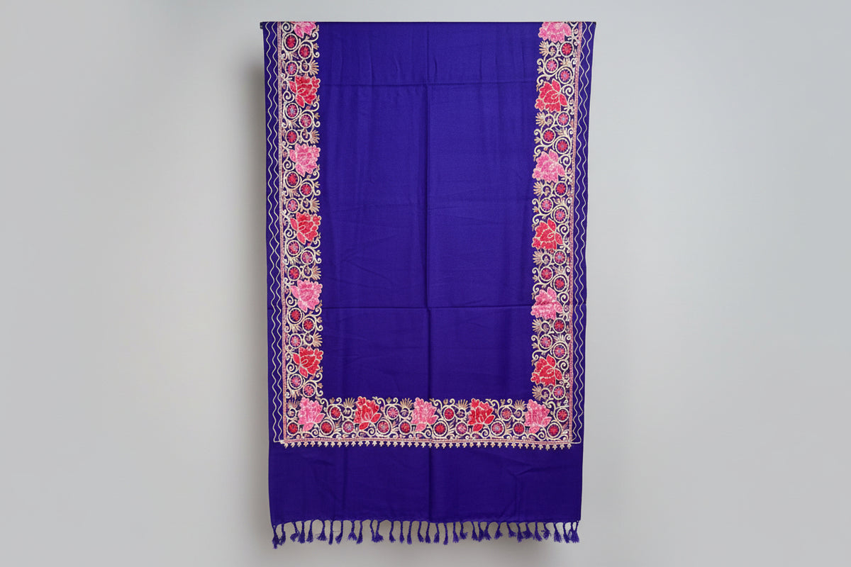 A navy blue shawl with floral patterns draped over a mannequin next to a black handbag on a small table against a marble wall.