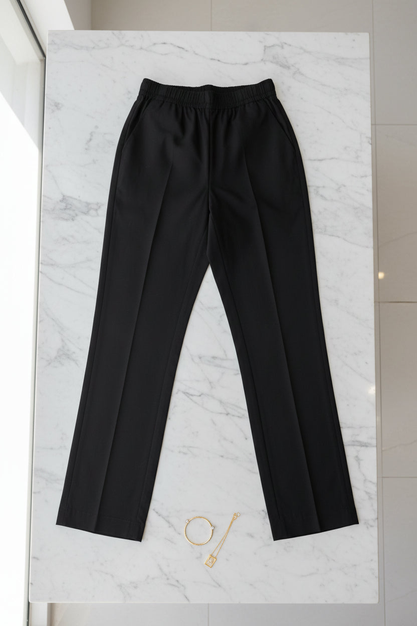 A pair of black pants hanging on a gold-framed garment rack in an indoor setting.