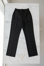 A pair of black pants hanging on a gold-framed garment rack in an indoor setting.