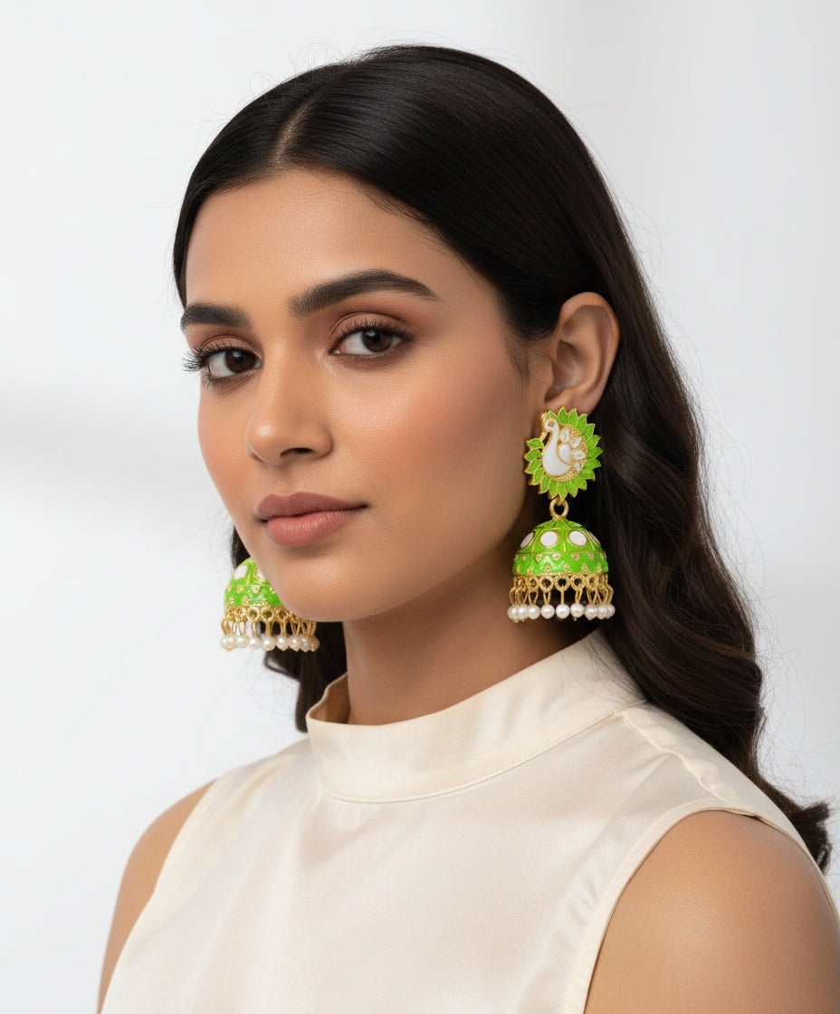 A pair of gold-plated Meenakari peacock Jhumka earrings with green and white enamel detailing, displayed on a black stand.