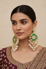 A pair of gold-plated Parul Pearl kundun earrings with intricate designs and drop-shaped pearls, displayed on a stand.