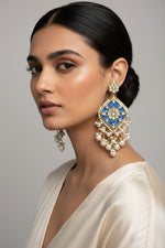 A pair of gold-plated Parul Pearl kundun earrings with intricate designs and drop-shaped pearls, displayed on a stand.