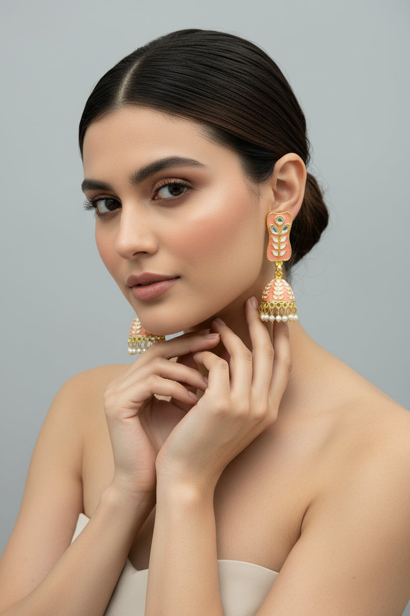 A pair of gold-plated Peach colour Meenakari drop Jhumka earrings displayed on a stand, featuring intricate designs and studded with stones.