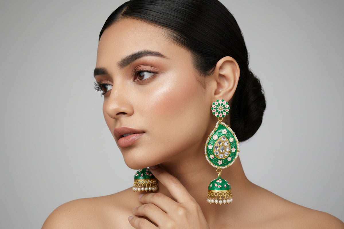 A pair of gold-plated green Meenakari long Jhumka earrings with green enamel paint and nano pearl drops, displayed on a stand.