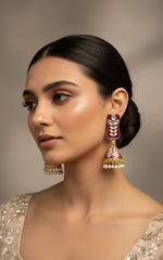 A pair of gold-plated purple colour Meenakari drop Jhumka earrings displayed on a stand, featuring intricate designs and studded with stones.