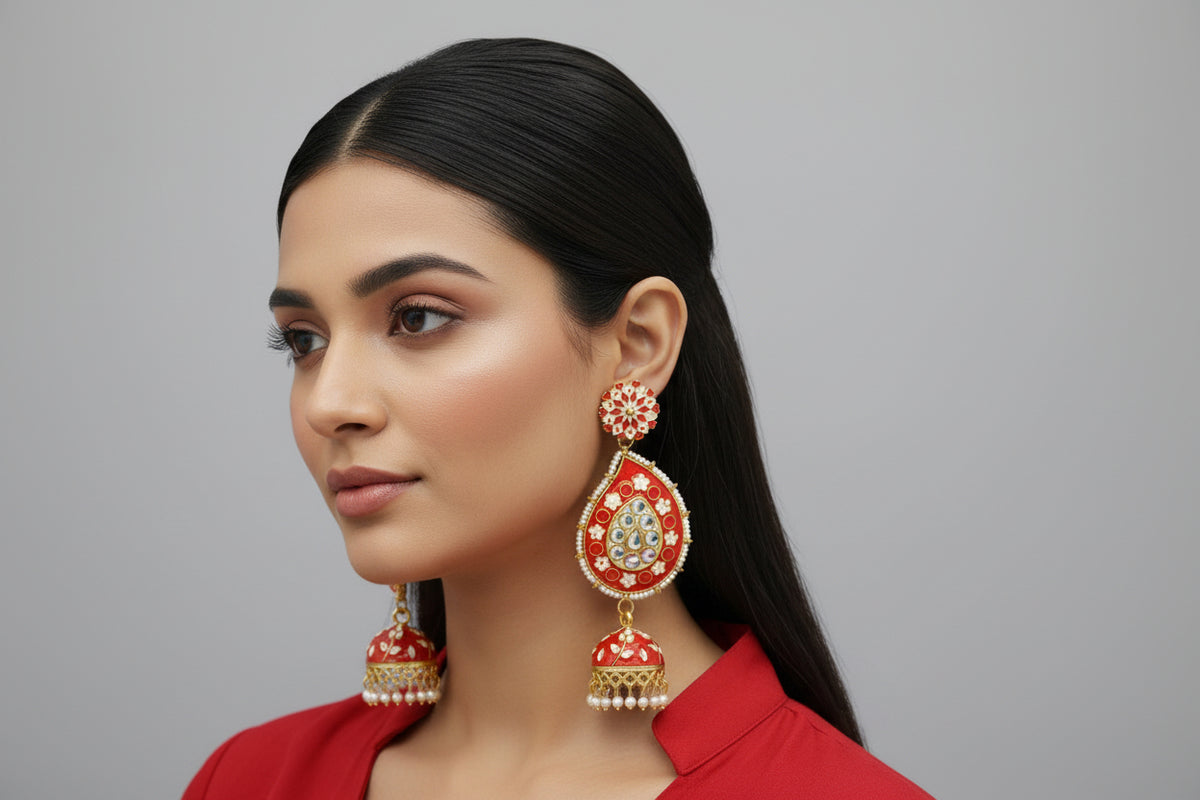 A pair of gold-plated red Meenakari long Jhumka earrings with red enamel paint and nano pearl drops, displayed on a stand.