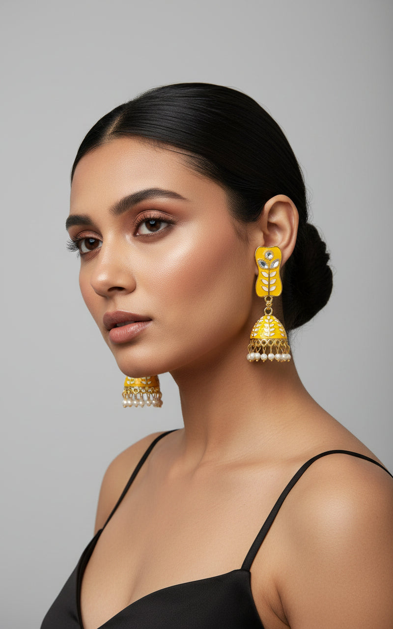 A pair of gold-plated yellow colour Meenakari drop Jhumka earrings displayed on a stand, featuring intricate designs and studded with stones.