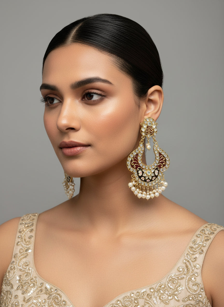 A pair of gold-toned chandbali earrings with maroon and black meenakari and kundan studded details along with pearls.