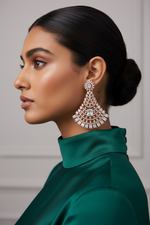 A woman in profile wearing a large, ornate gold-toned statement earring with clear stones and a green satin high-neck top.