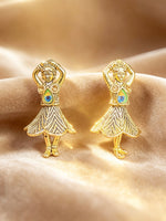 A pair of gold-toned dancer earrings with blue teardrop gemstones, displayed on a soft beige satin fabric background.