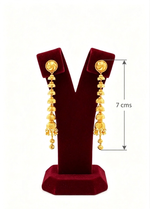 A pair of gold-toned dangle earrings displayed on a dark red velvet jewellery stand against a white background, with a vertical measurement arrow and text indicating 7 cm length.