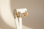 A pair of golden square-shaped hoop stud earrings densely set with small, sparkling crystals.