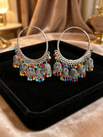 A pair of large silver-toned hoop earrings with ornate dangling filigree charms and small multi-coloured beads, displayed on a black velvet jewellery tray.