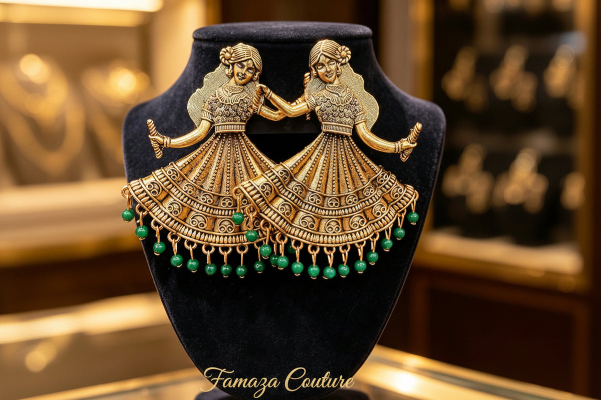A pair of ornate gold-toned earrings shaped like two dancing figures in traditional dress, with dangling green bead accents, displayed on a black velvet jewellery bust.