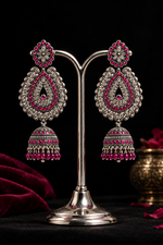 A pair of oxidised tone tear drop earrings with hot pink nano stones and hangings are displayed on a silver stand. 