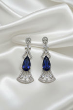 A pair of silver-toned Art Deco style drop earrings with marquise-cut deep blue gemstones and pavé-set clear accent stones, displayed on a black card against a dark background.