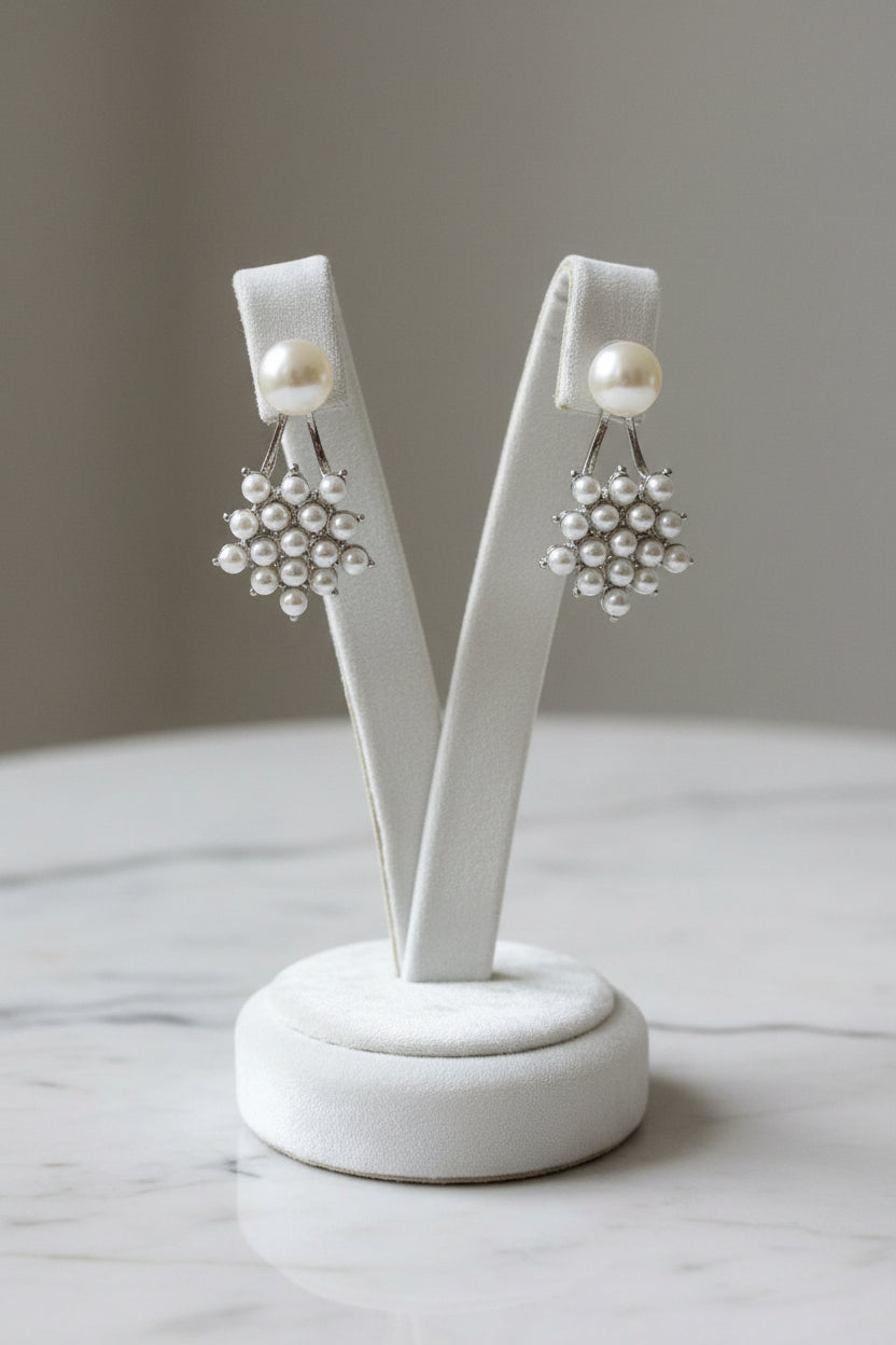 A pair of silver-toned cluster earrings with a single white pearl hanging from each, displayed on a light grey wood-grain surface.