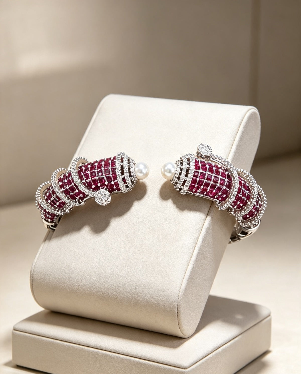 A pair of silver-toned cuff-style earrings with rows of deep red gemstones and small white pearls, displayed on a cream jewelry stand against a warm beige background.
