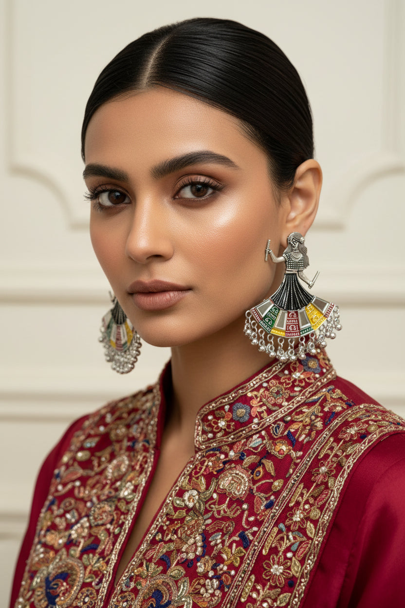 A pair of silver-toned dholak dancer earrings displayed on a black velvet jewelry box, surrounded by orange marigold flowers on a white marble surface.