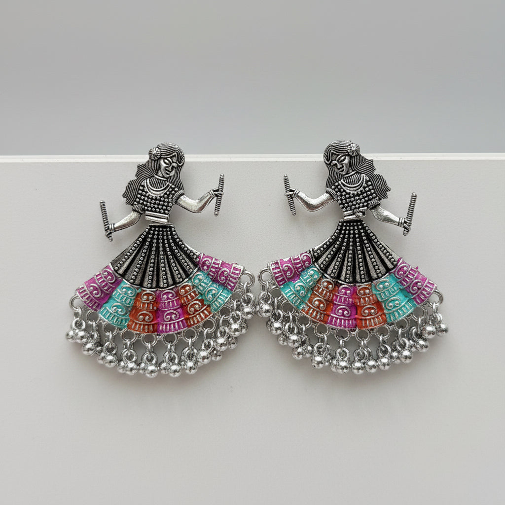 A pair of silver-toned dholak dancer earrings with multi-coloured beaded skirts, displayed on a white marble surface.