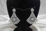 A pair of silver-toned, tiered chandelier-style earrings with clear stones and a central blue stone, displayed on a black velvet jewellery bust inside a shop.