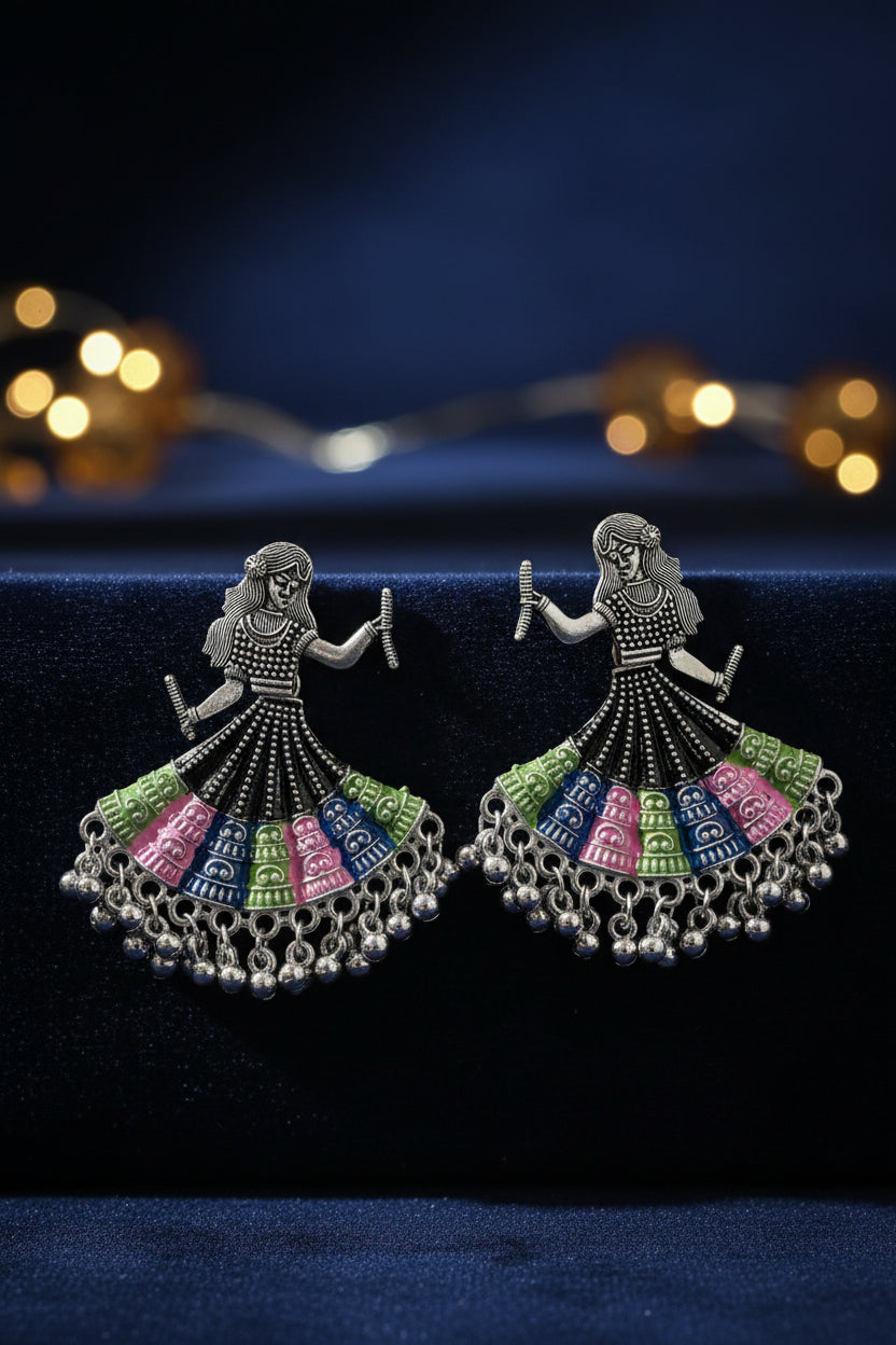 A pair of silver toned metal oxidised earrings design is showing a woman is playing dandiya in navratri lehnga choli traditional dress for navratri. 