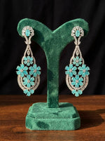 A pair of turquoise petal chandelier earrings displayed on a green stand.