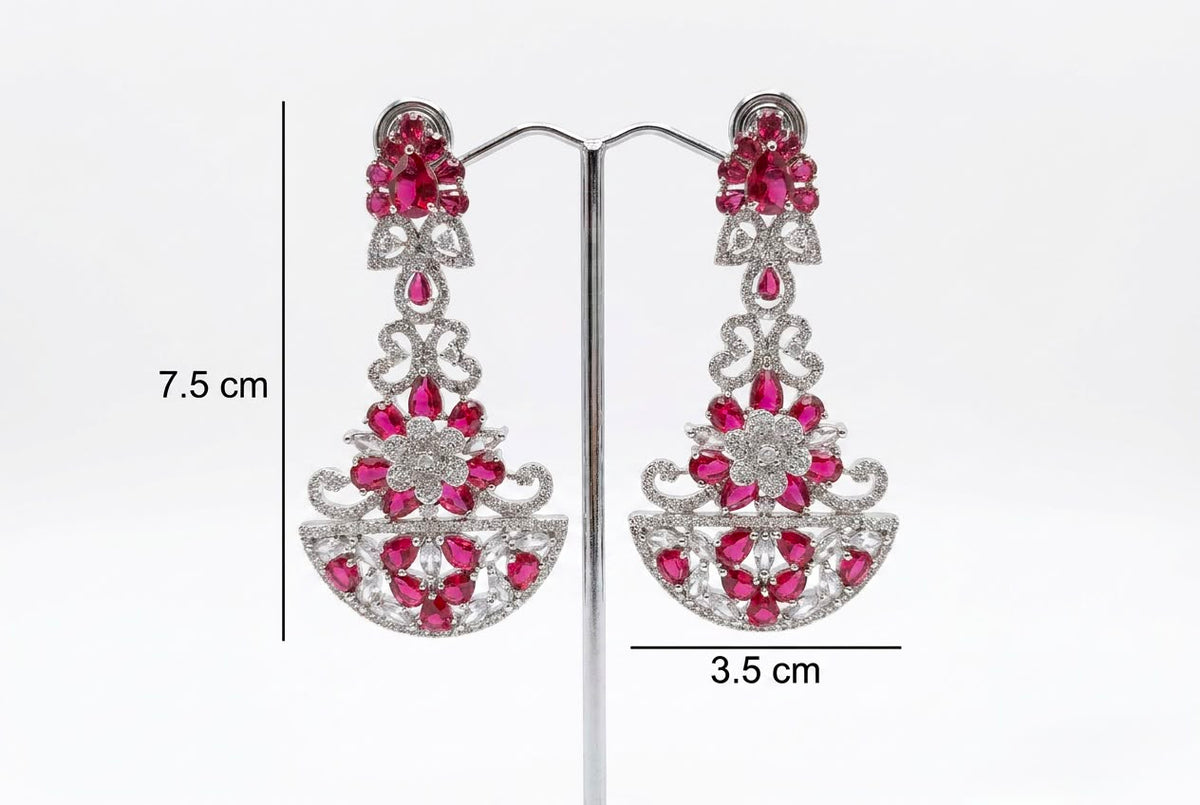 A pair of vibrant fuchsia and clear crystal chandelier earrings, 7.5 cm in length, displayed on a jewelry stand.