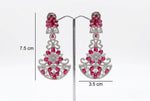 A pair of vibrant fuchsia and clear crystal chandelier earrings, 7.5 cm in length, displayed on a jewelry stand.