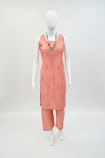 A peach-pink textured sleeveless dress displayed on a white mannequin torso in a retail store setting, with other clothing items and store fixtures visible in the background.